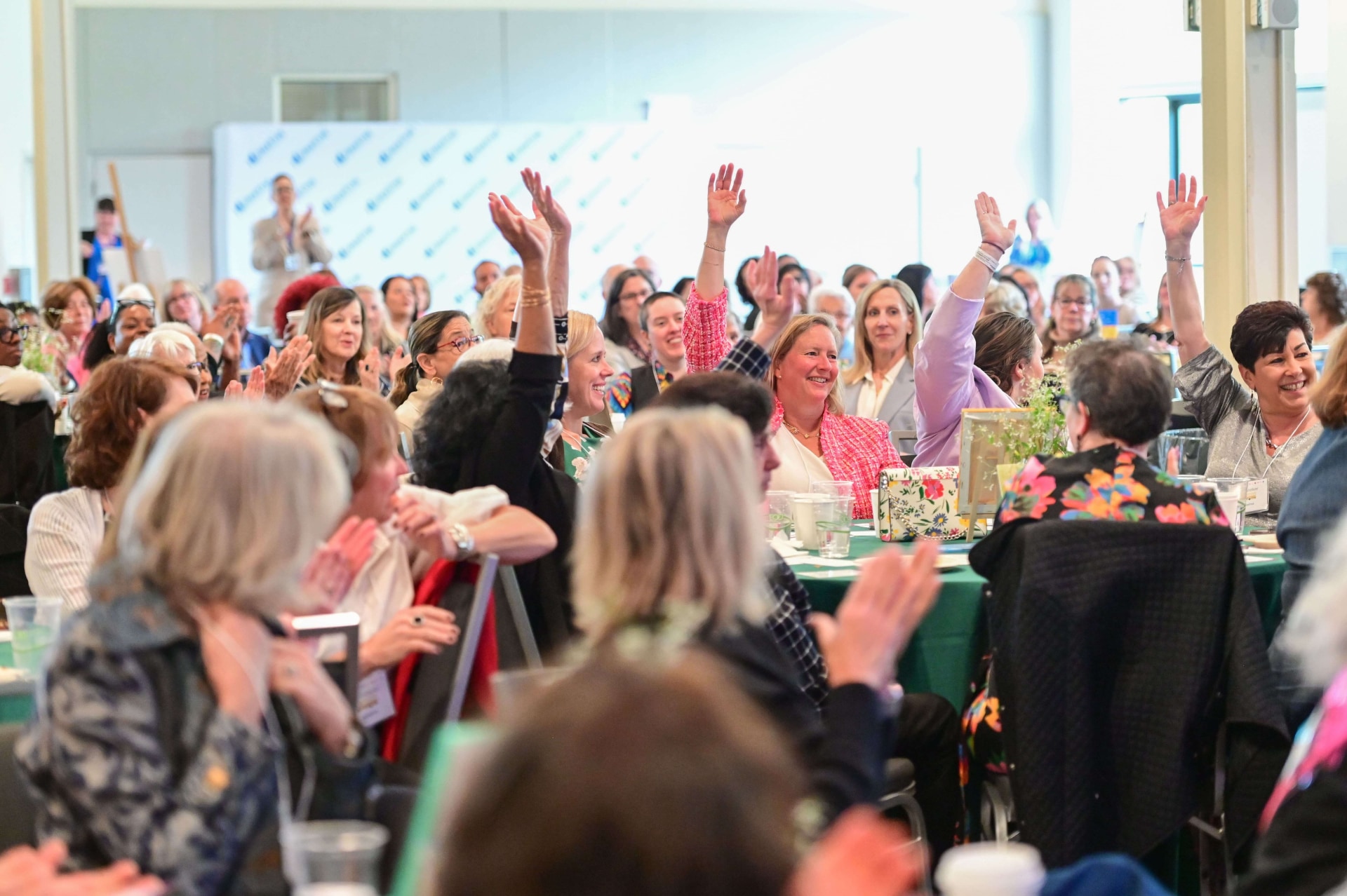 a group of people sitting at a table raising their hands